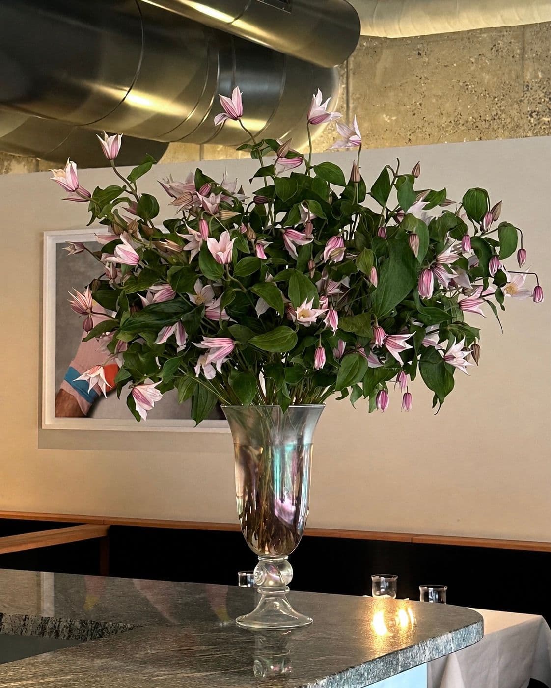 Pale pink clematis in a tall glass vase on a stone bar